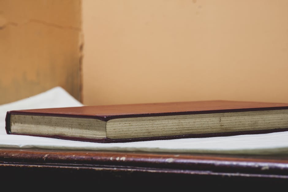 Close-up of a vintage book with a brown cover on a wooden table against a neutral wall.