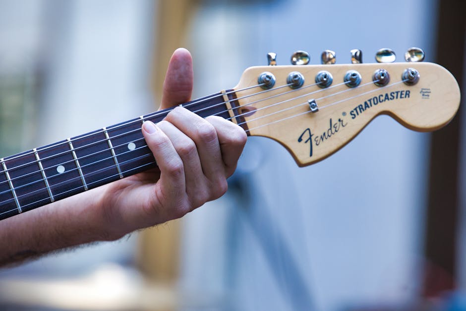 Close-up view of a guitarist's hand playing a Fender Stratocaster outdoors.
