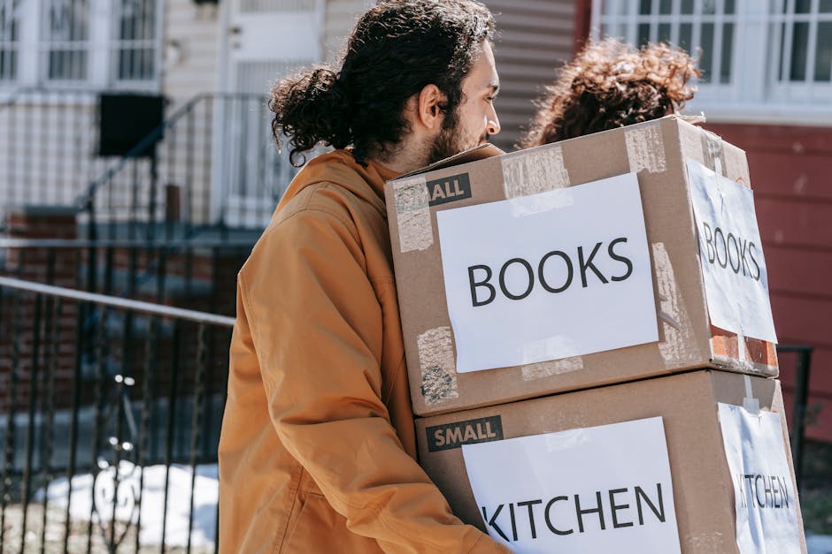 A couple carrying labeled boxes outside, symbolizing moving to a new home.