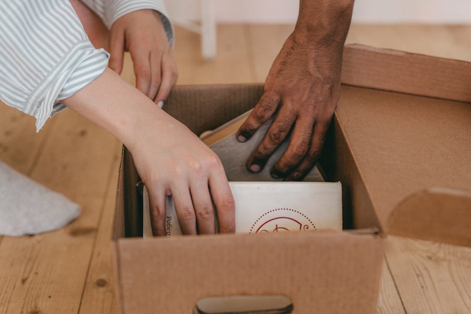 Close-up of two diverse hands organizing books in a cardboard box indoors.