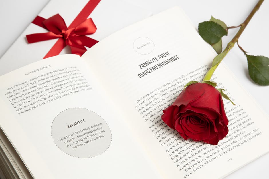 An open book with a red rose and a tied gift box next to it, conveying romance or celebration.